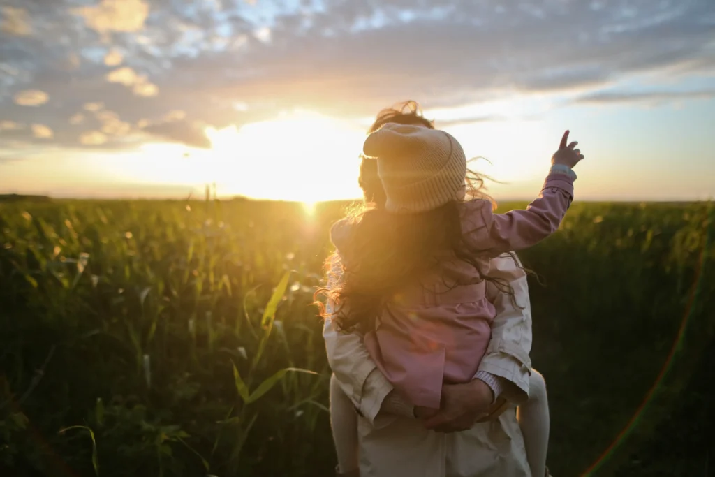 A parent holding their child during a sunset.