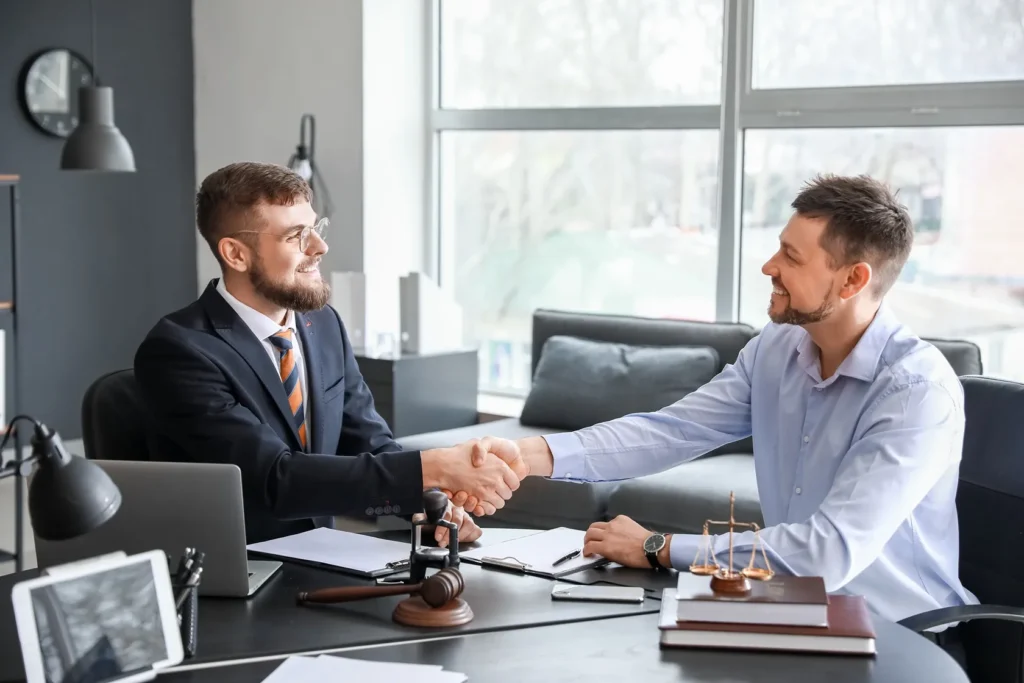 A lawyer and client shaking hands in a an office setting.